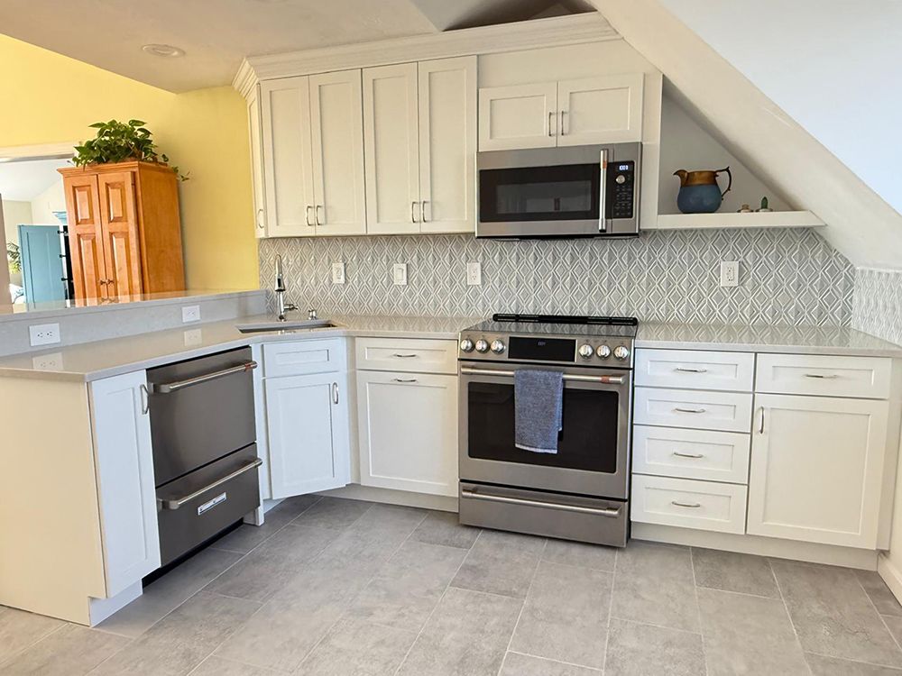 A bright kitchen with white cabinets, stainless steel appliances, and gray tile flooring.