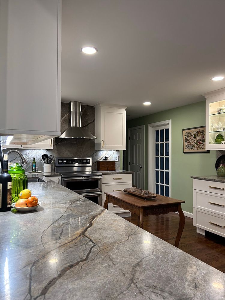 Modern kitchen with gray countertop, white cabinets, stainless steel appliances, and green walls.