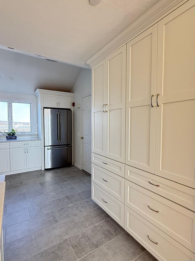 White kitchen with tall cabinets, stainless steel fridge, and gray tiled floor.