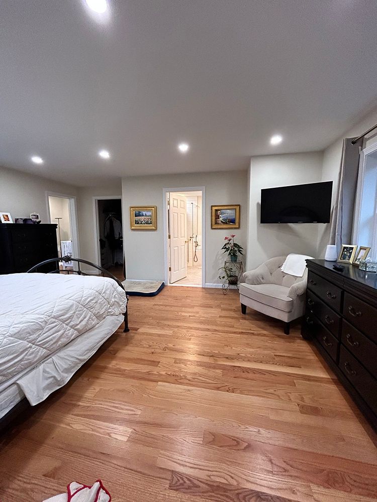 Bedroom with hardwood floors, bed, dresser, chair, and TV on the wall. Doorways lead to a closet and bathroom.