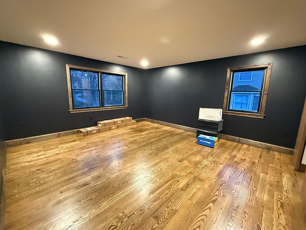 Empty room with wood floor, dark blue walls, two windows, and recessed lighting.