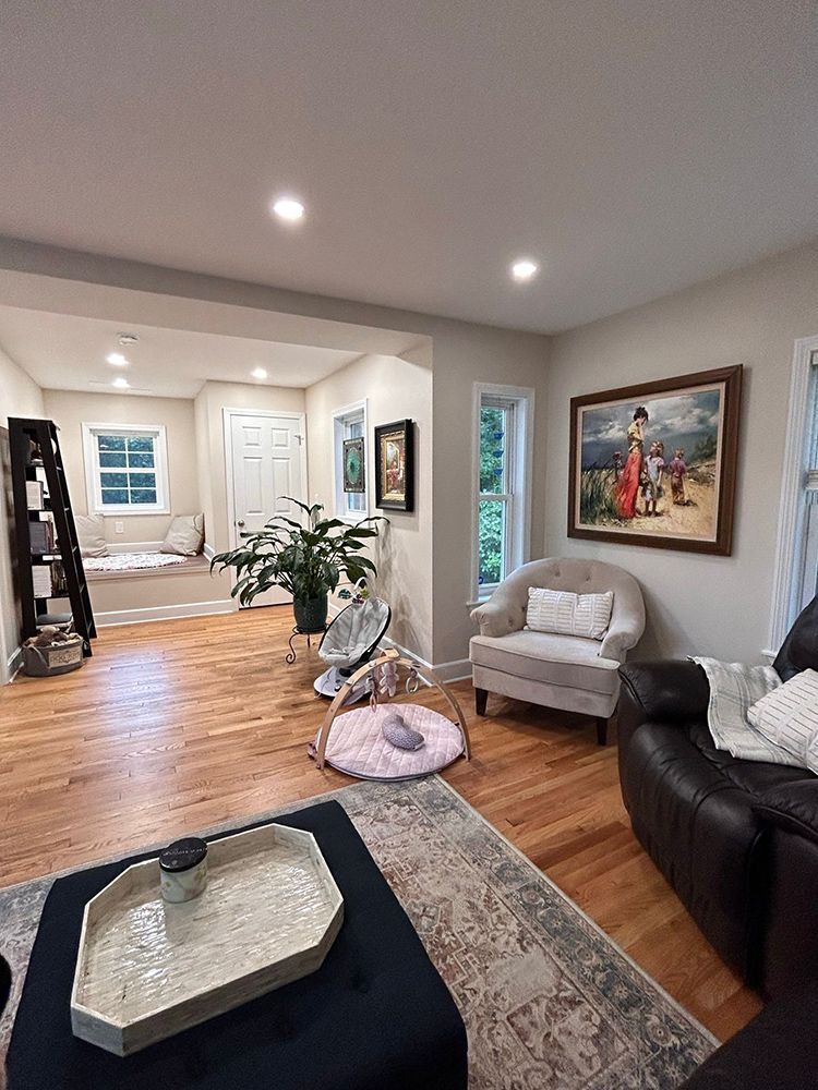 Living room with hardwood floors, beige walls, and a framed painting. Includes a reading nook, armchair, and dark blue ottoman.