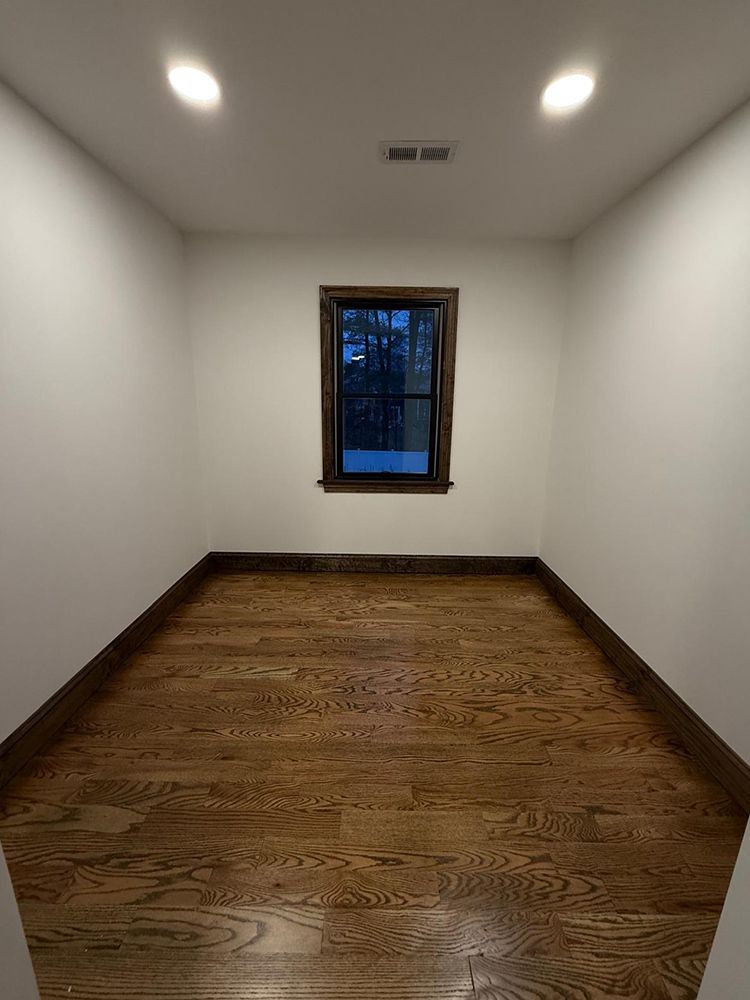 Empty room with hardwood floor, small window, white walls, and dark trim.