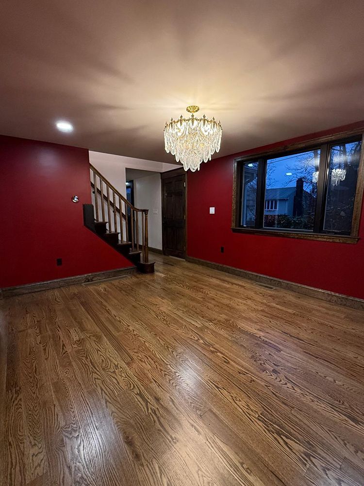 Living room with red walls, wooden floors, a chandelier, and a staircase.