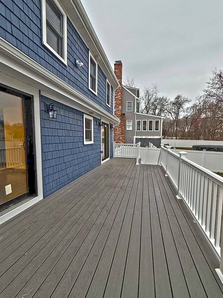 Blue-sided house with a gray deck and white railing, set against a cloudy sky.