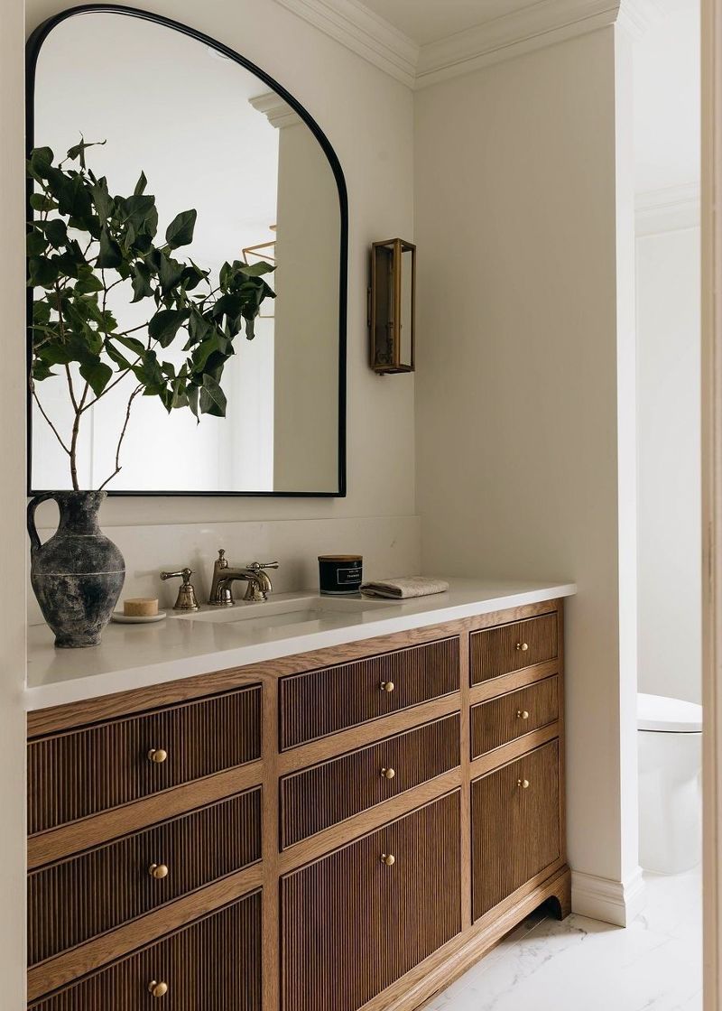 A bathroom with a sink , mirror and wooden cabinets.
