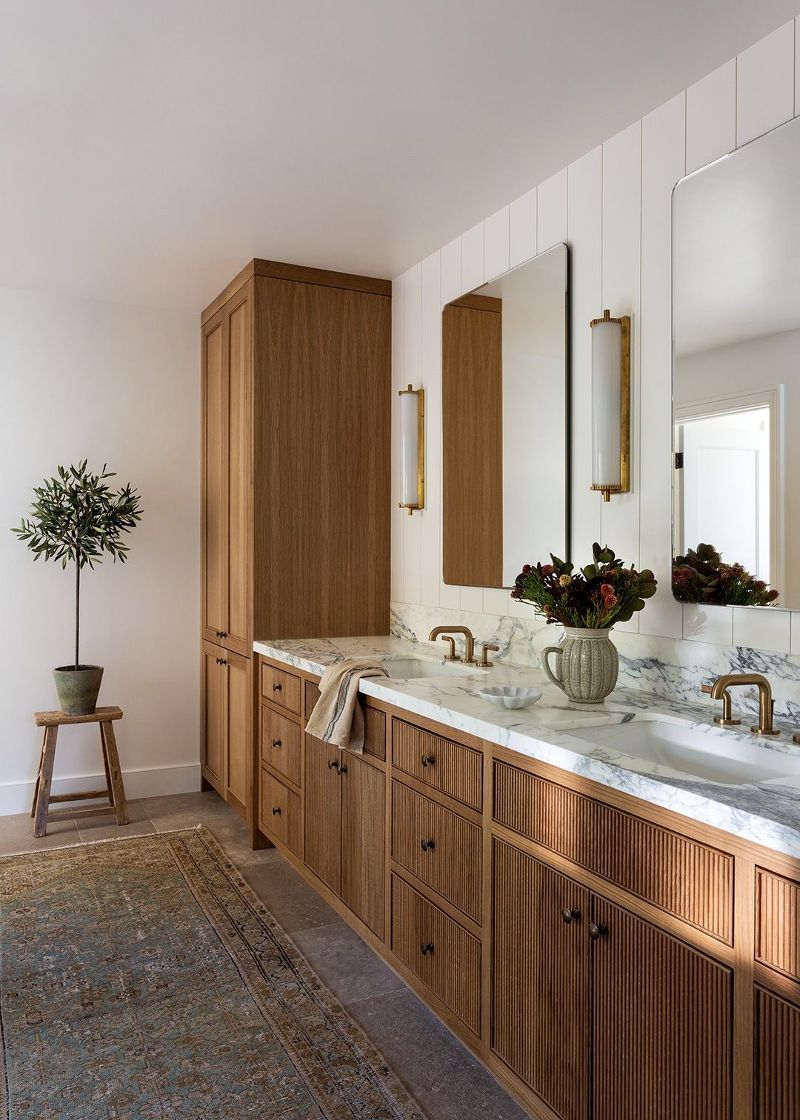 A bathroom with two sinks , a mirror , and wooden cabinets.