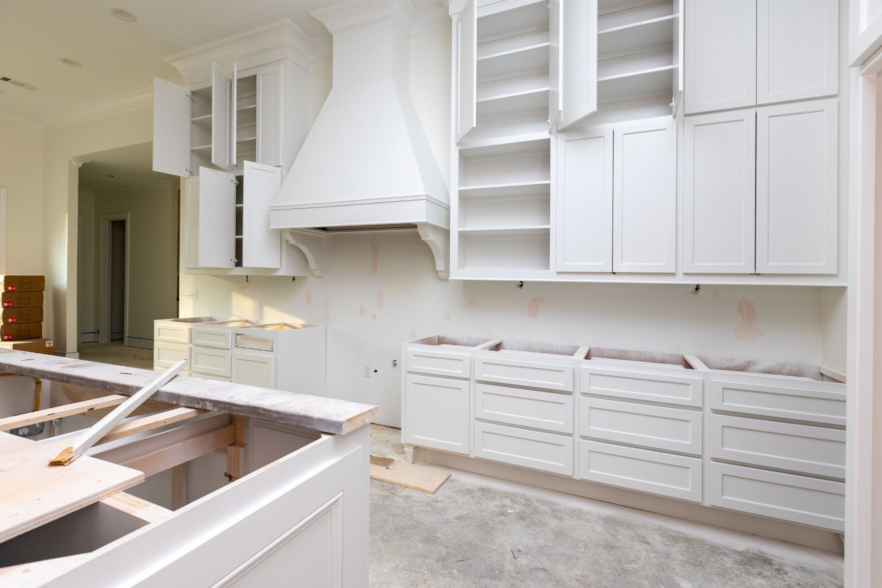 A kitchen under construction with white cabinets and a hood.