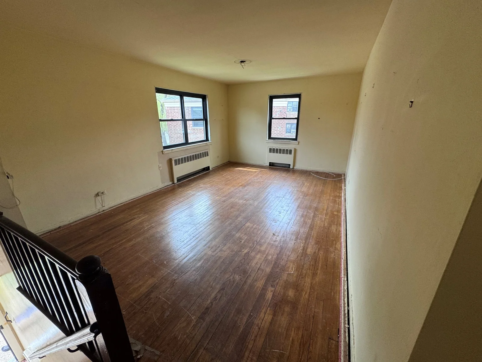 Empty room with wood floors, two windows, and a staircase. Beige walls.