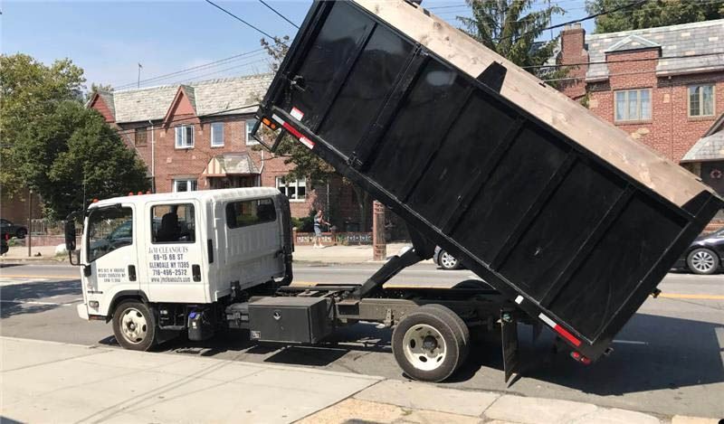 White dump truck with a raised black bed on a city street, unloading debris.