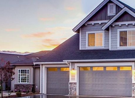 A large house with two garage doors and a sunset in the background.