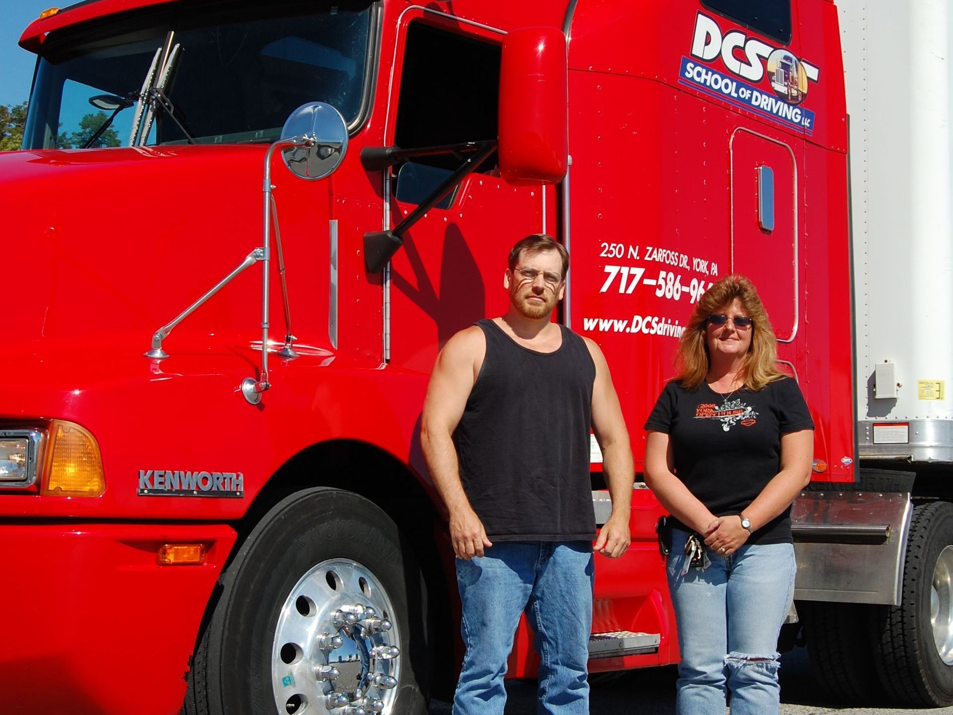 A man and a woman standing in front of a red truck that says dcsst