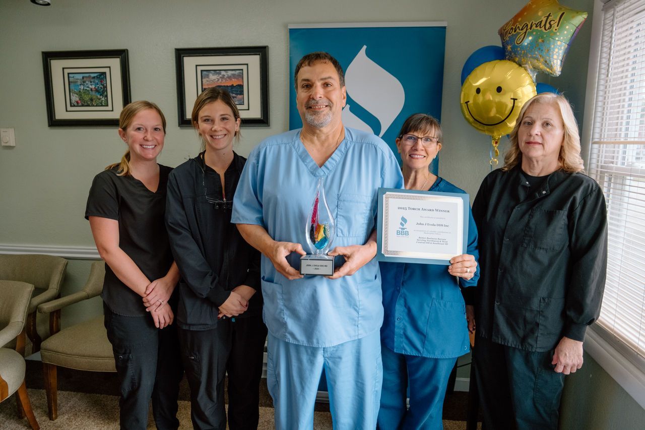 A man in scrubs holds an award, smiling, with four colleagues in an office. They are holding balloons and a sign.
