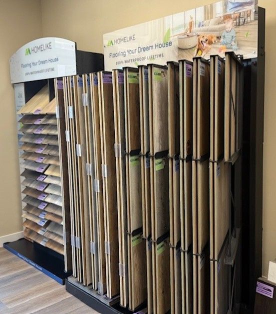 Displays of various wood and laminate flooring samples in a showroom, arranged in tiered shelves and pull-out racks.