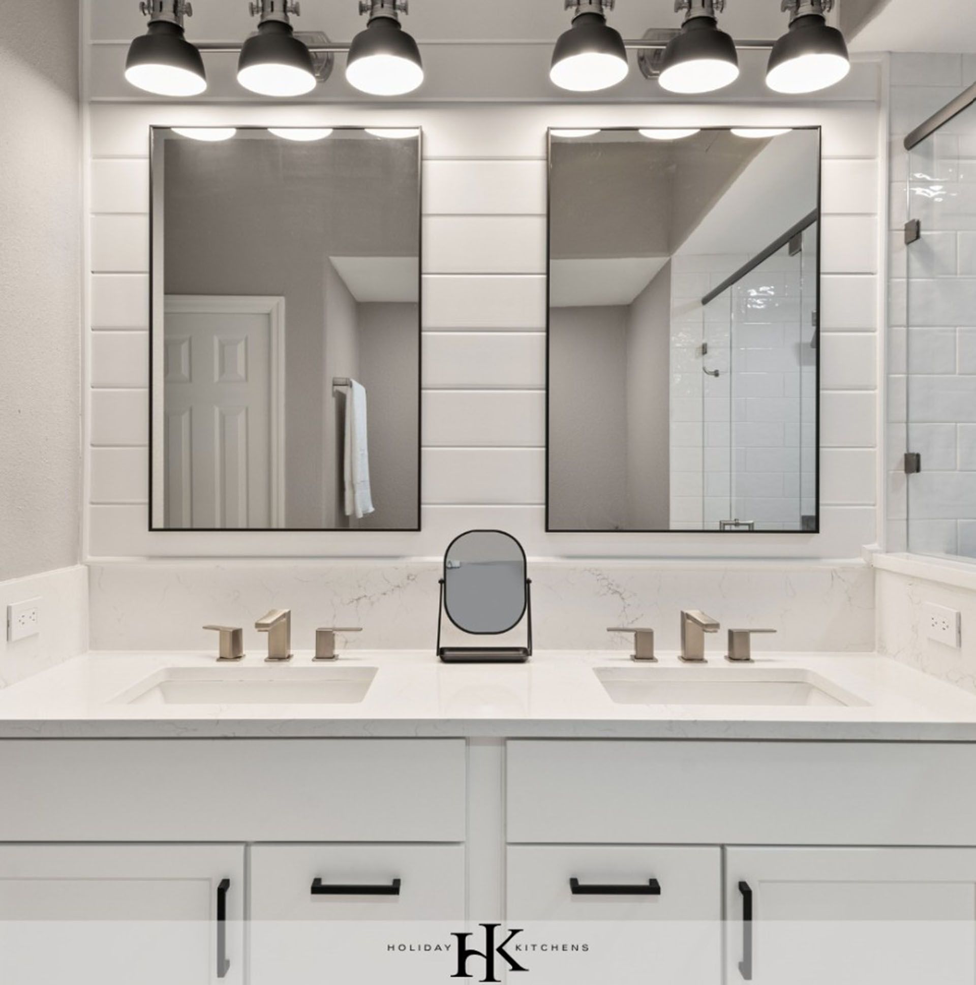 A double vanity bathroom with white cabinets, marble countertops, two rectangular mirrors, and black light fixtures.