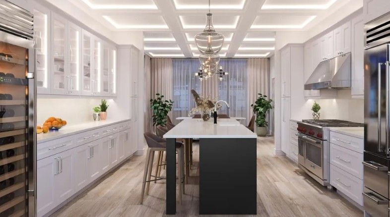 A modern white kitchen with a dark central island, light wood floors, coffered ceilings, and a hanging pendant light.