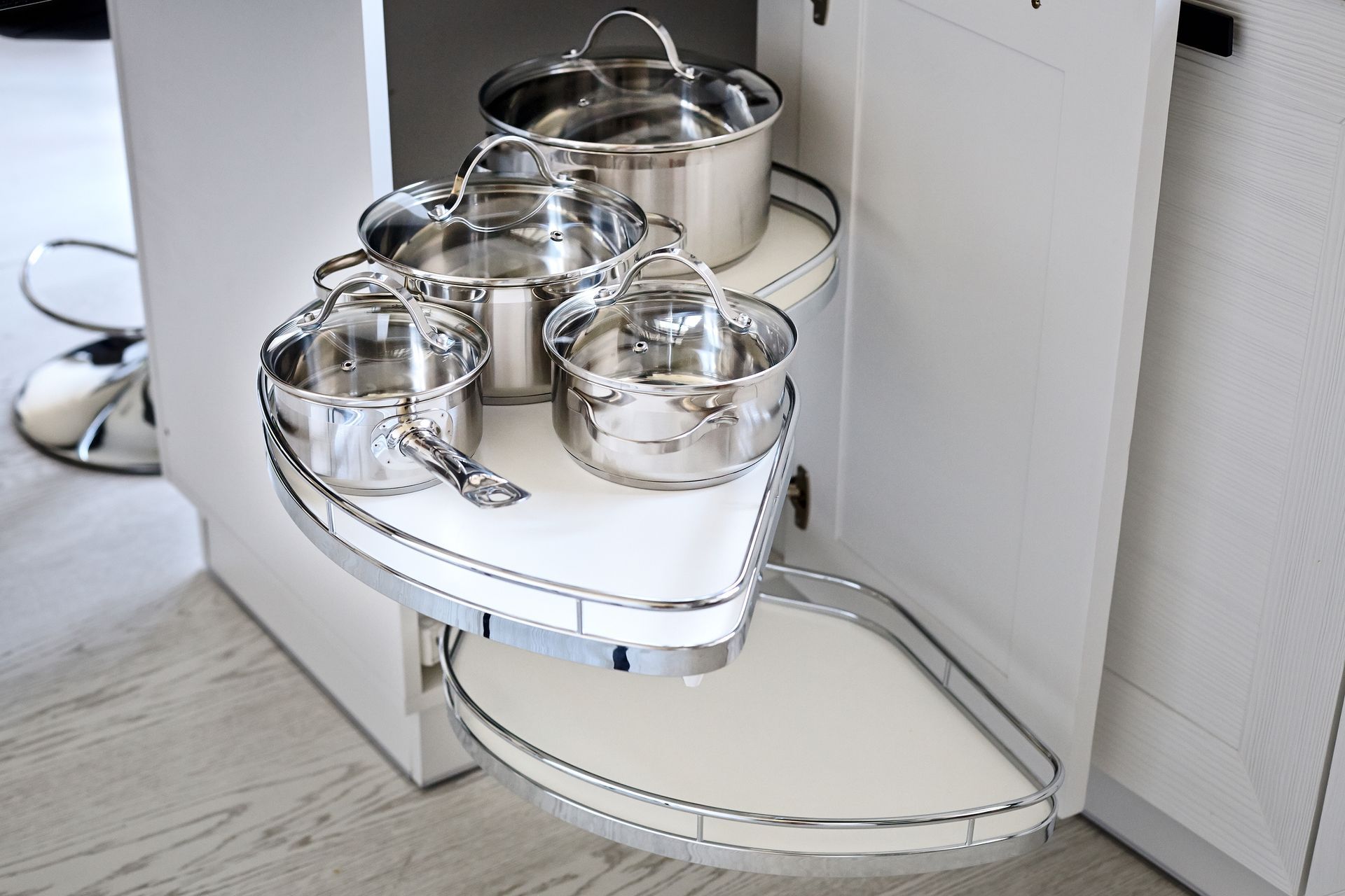 A white pull-out corner kitchen cabinet shelf containing stainless steel pots and pans.