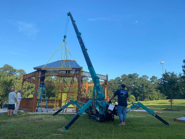 A crane is being used to lift a gazebo in a park.