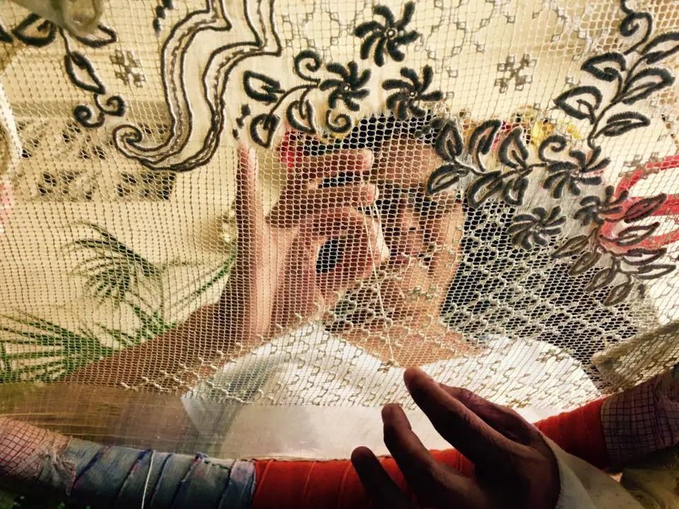 Person works on detailed embroidery, hands visible. Floral and leafy designs are prominent in the work.