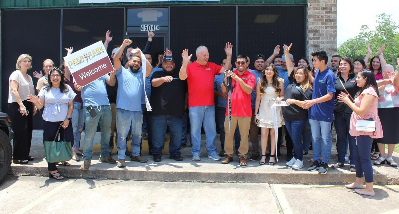 A group of people celebrate in front of a building. Many are cheering and have their arms raised. Two women on the right are handing something to a person.