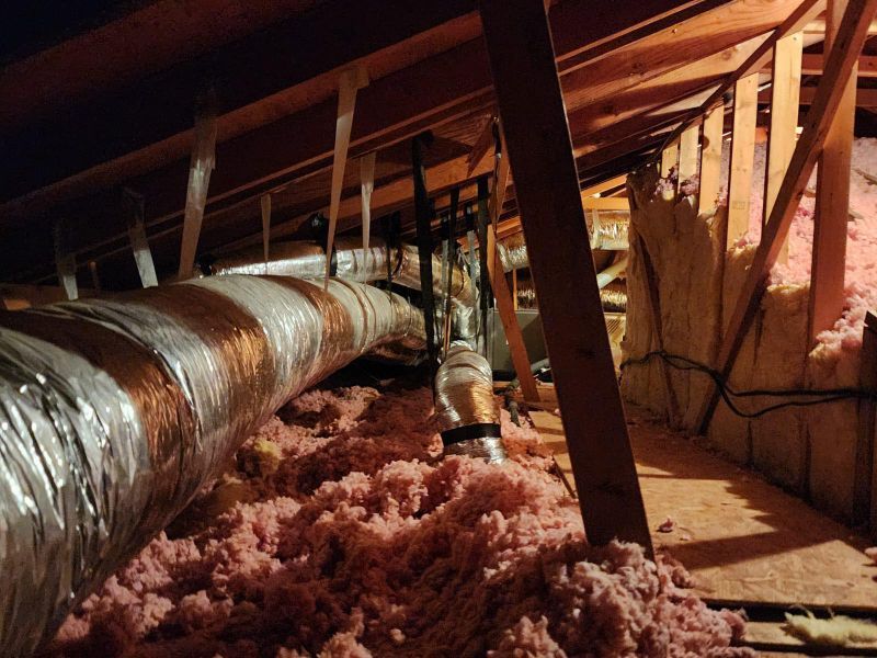 Attic with ductwork and pink insulation visible between wooden rafters. A silver and orange flexible duct is prominent.