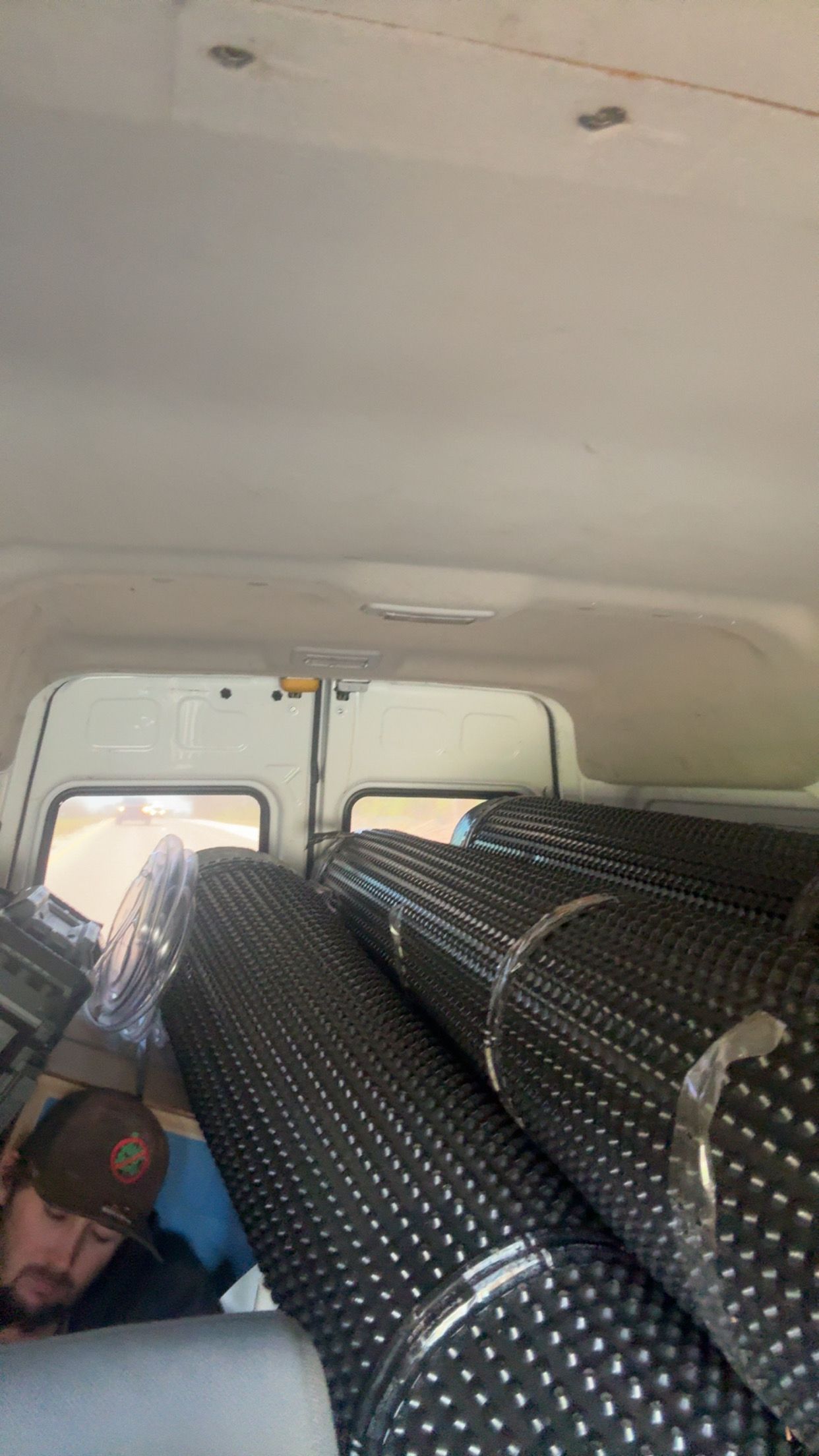 Interior of a van packed with rolled black mats or pipes, viewed from the back seat.