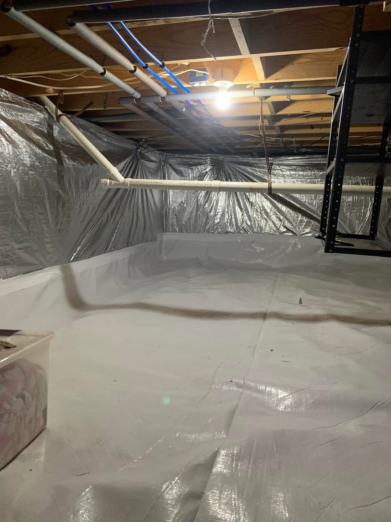 Large unfinished attic insulated with silver vapor barrier and exposed rafters under a bright work light.