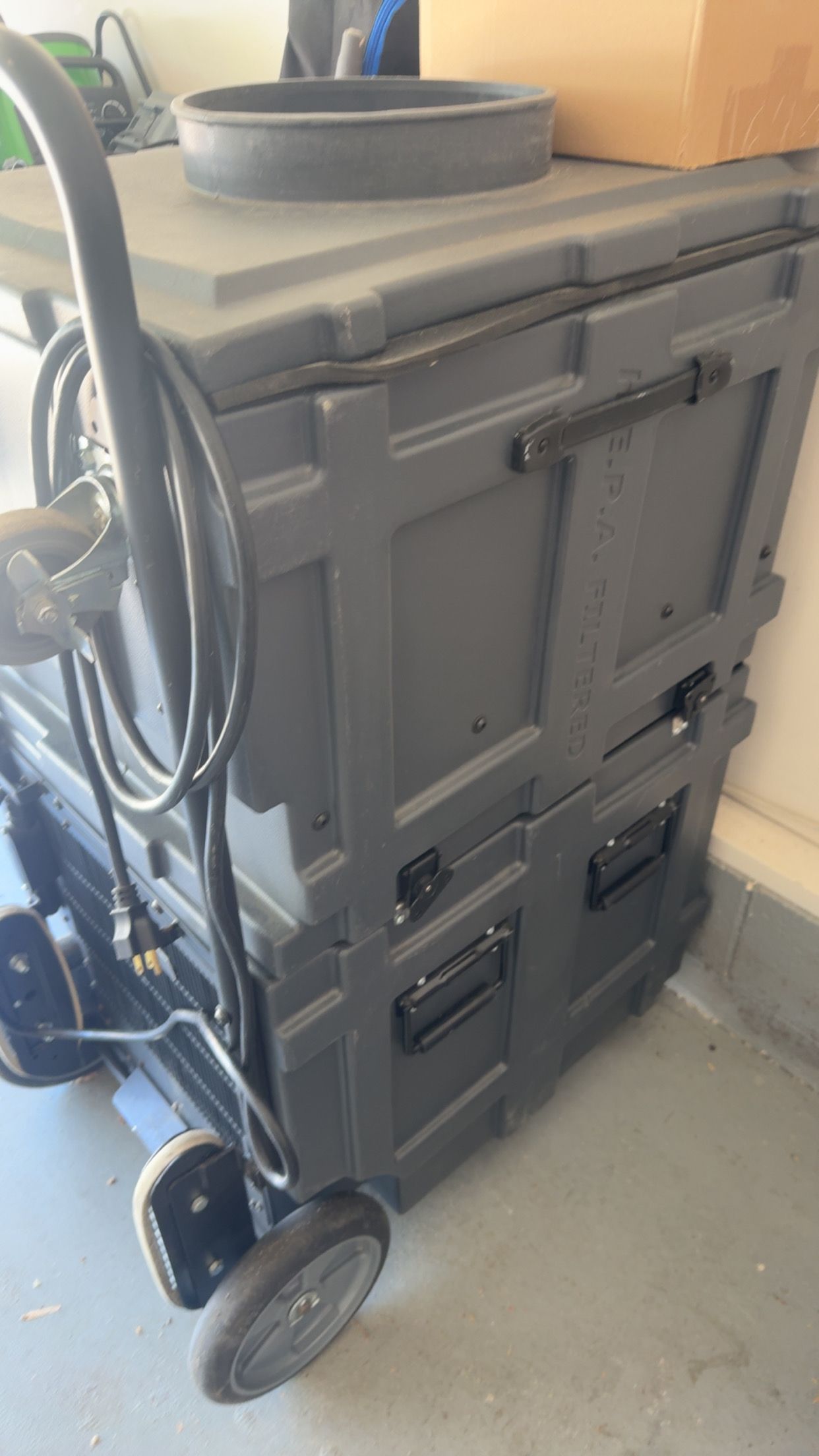 Large black rolling cart or cabinet with shelves and cords in a room corner
