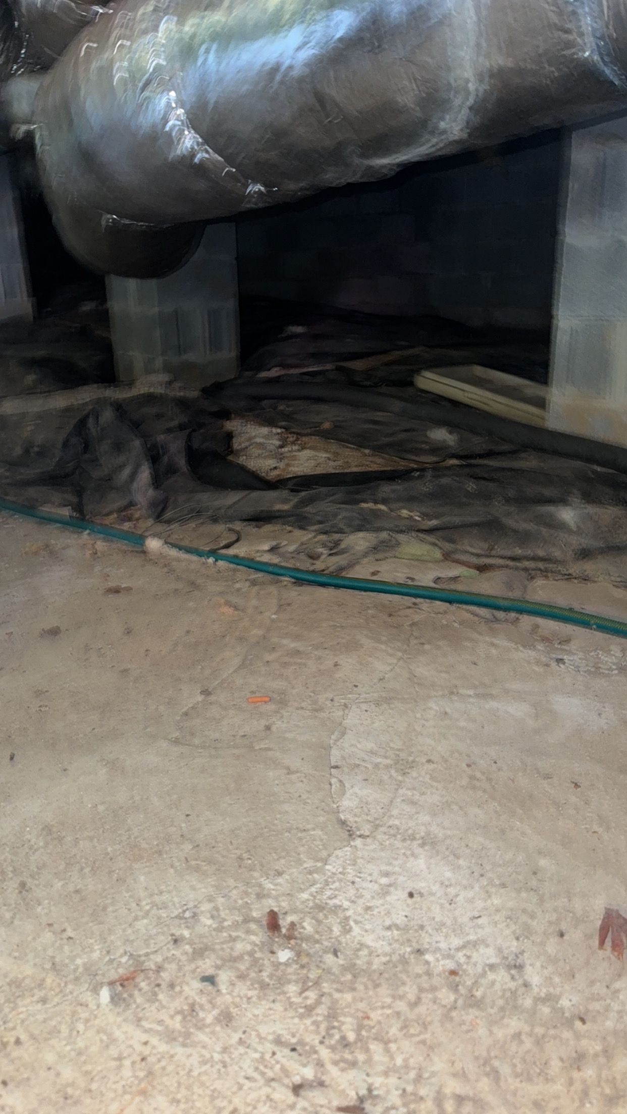 Large silver ductwork over a crawlspace with dirt floor and a green hose on the ground