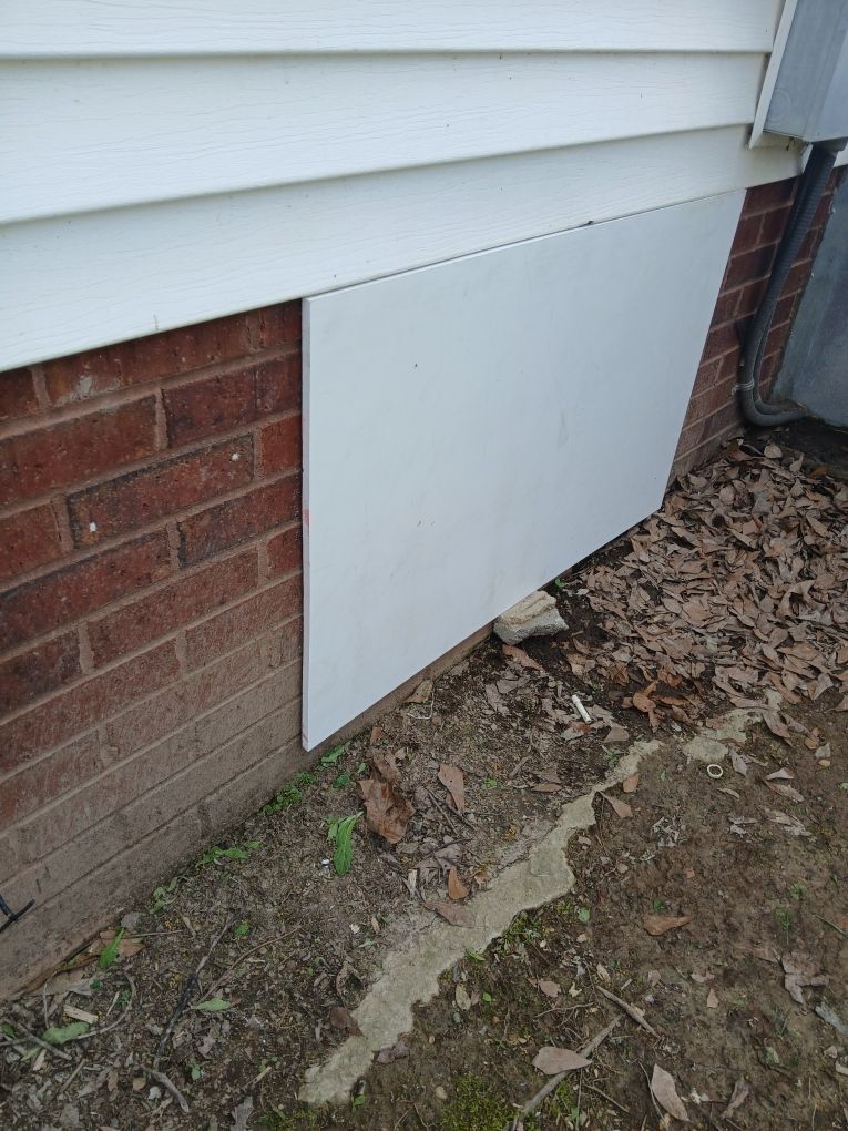 White foundation panel on a brick house exterior beside dirt and siding trim