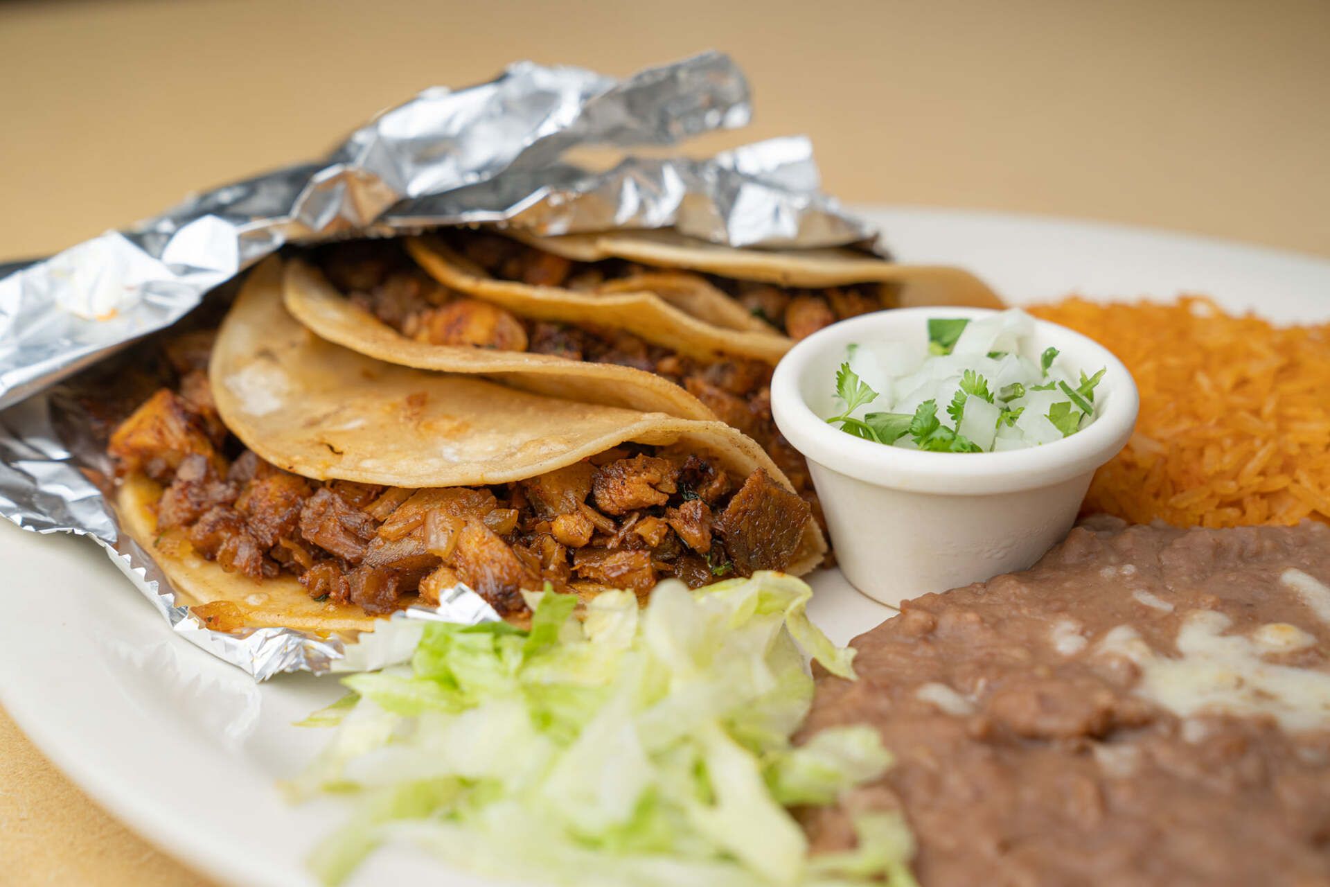 A white plate topped with tacos , beans , lettuce and rice.