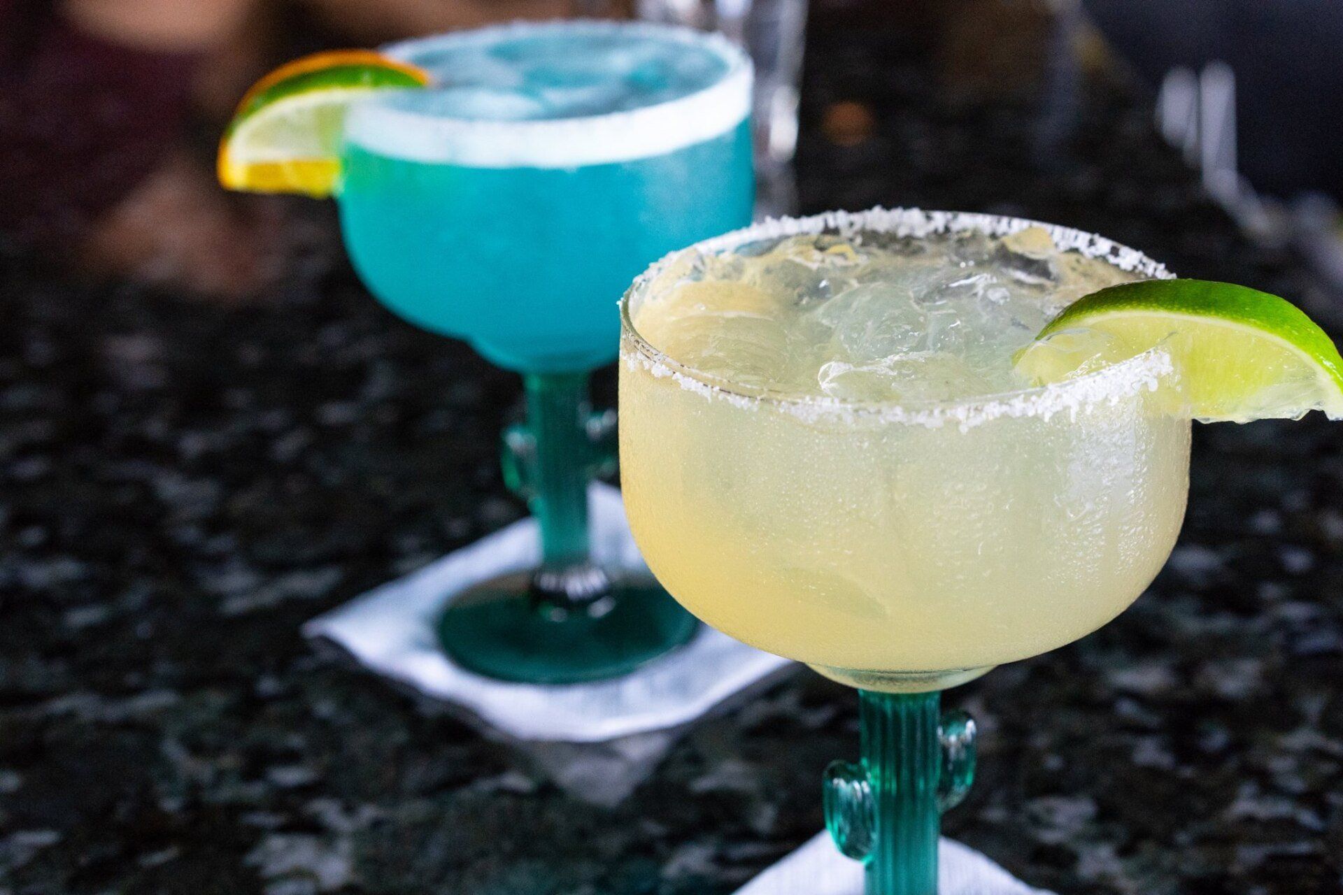 Two margaritas are sitting on a table next to each other.