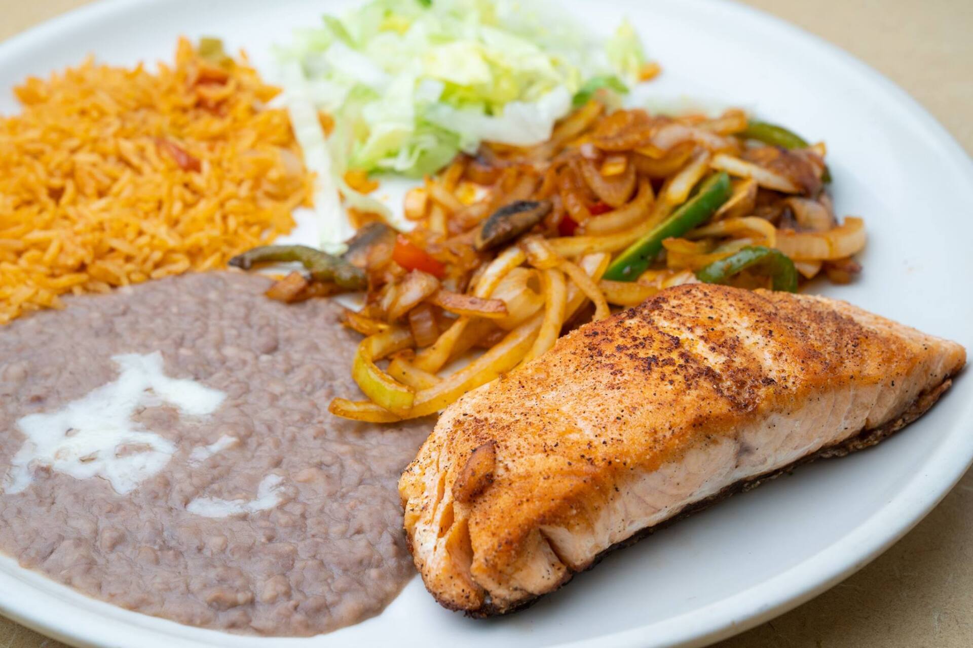 A white plate topped with a piece of salmon , beans , rice and vegetables.
