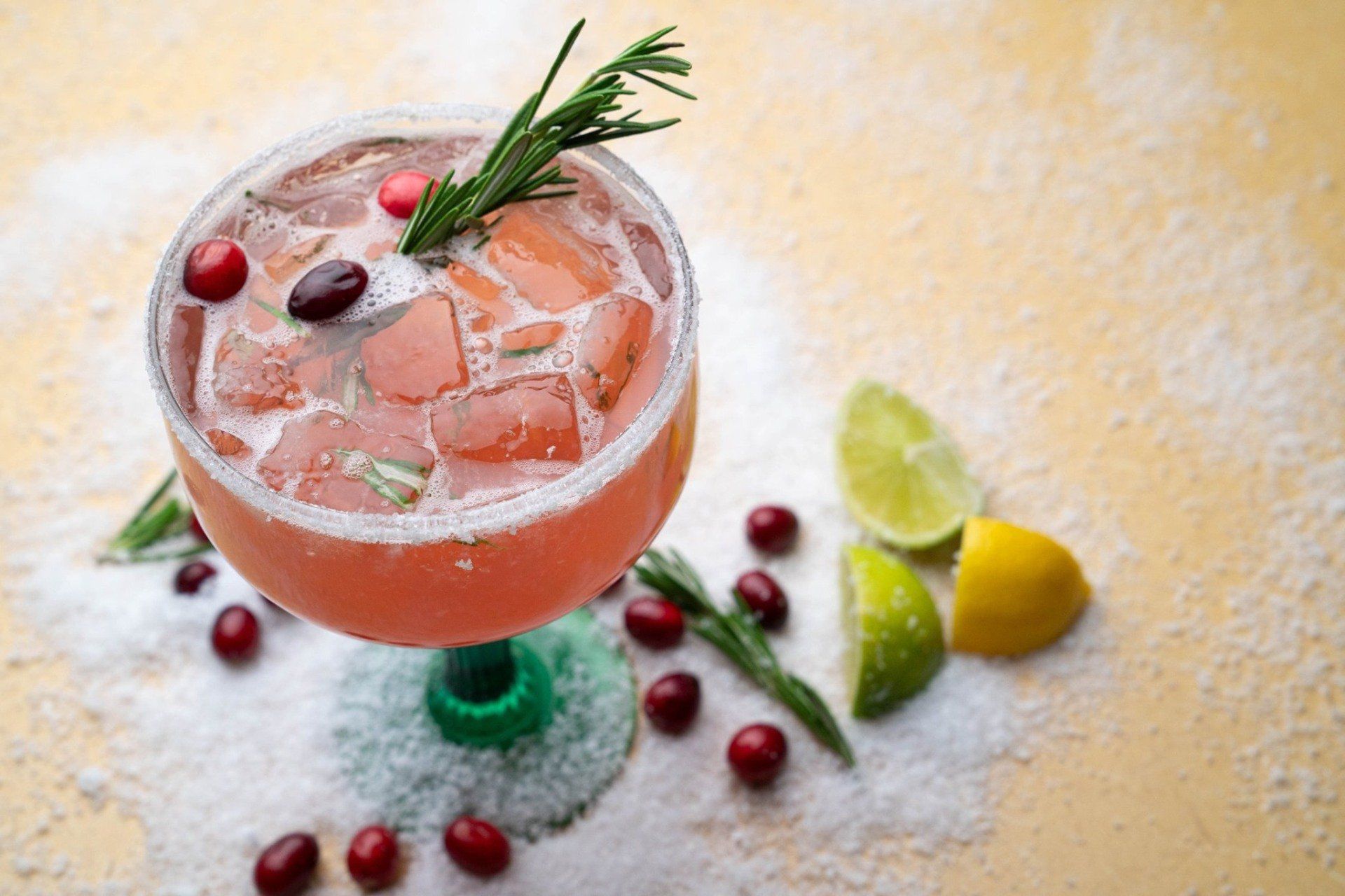 A close up of a margarita with cranberries and limes on a table.