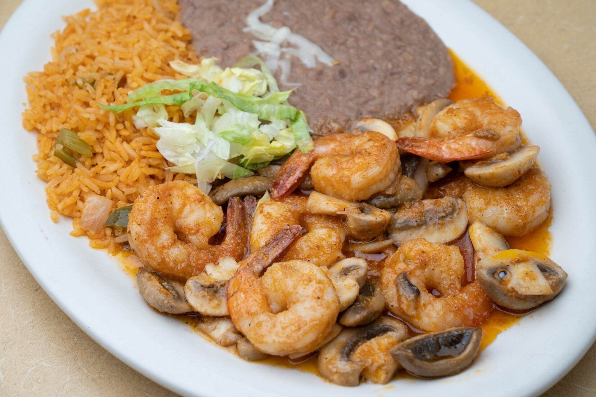A white plate topped with shrimp , mushrooms , rice and beans.