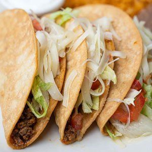 A close up of a plate of tacos with lettuce , tomatoes and onions.