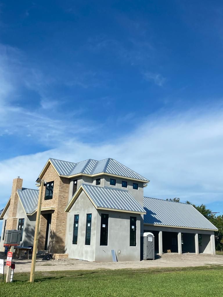 A house is being built with a metal roof and a for sale sign in front of it.