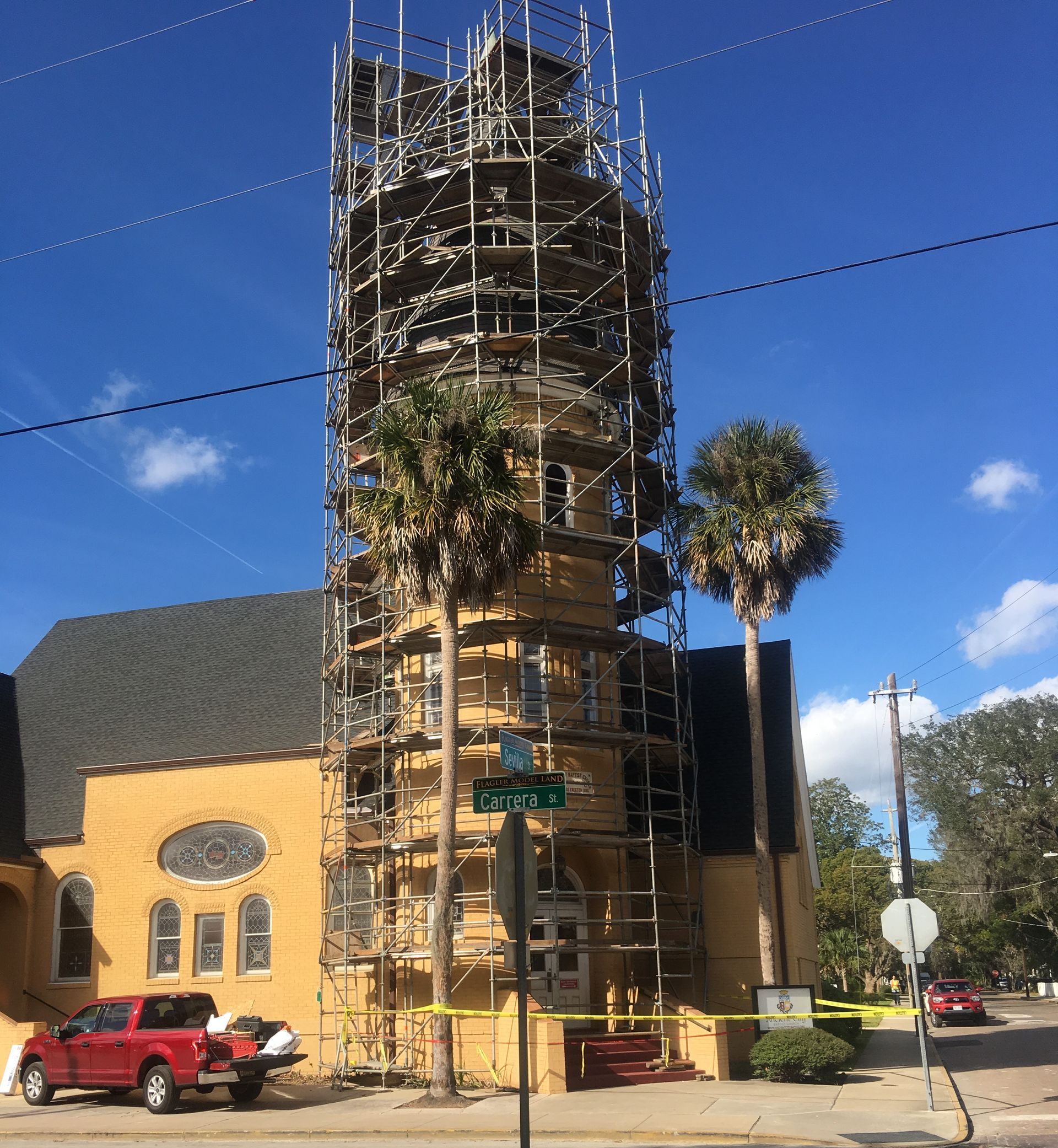 A yellow building with scaffolding around it and a red truck parked in front of it