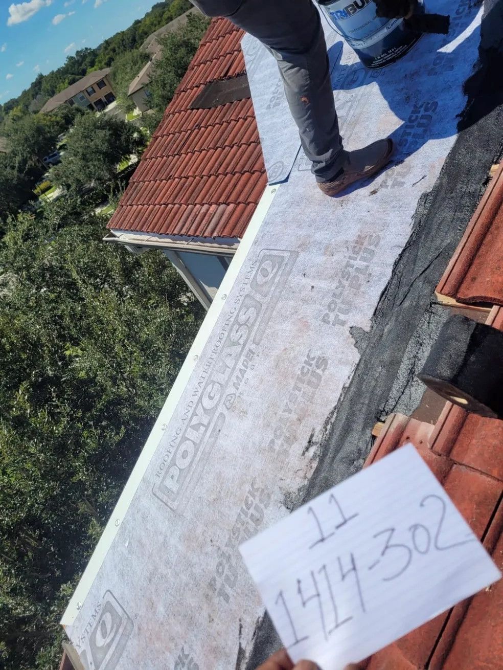 A person standing on top of a roof holding a piece of paper that says 1441-302
