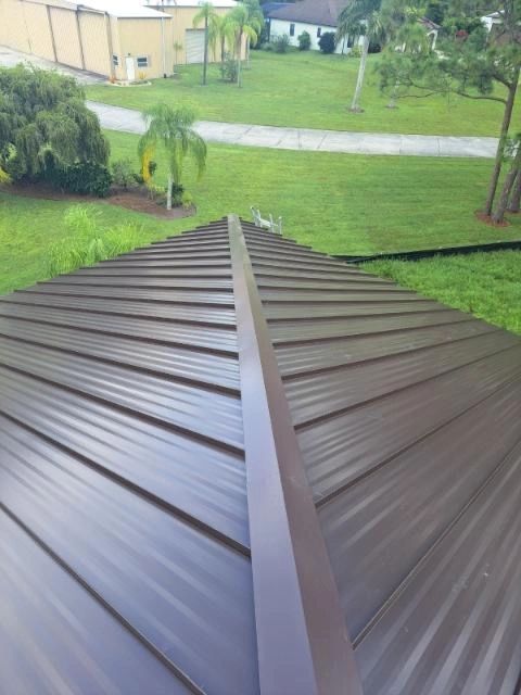 A close up of a metal roof with a grassy field in the background.