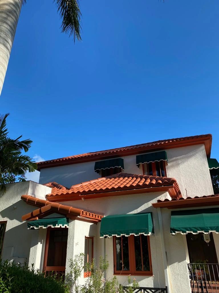 A white house with green awnings on the windows and a palm tree in the background.