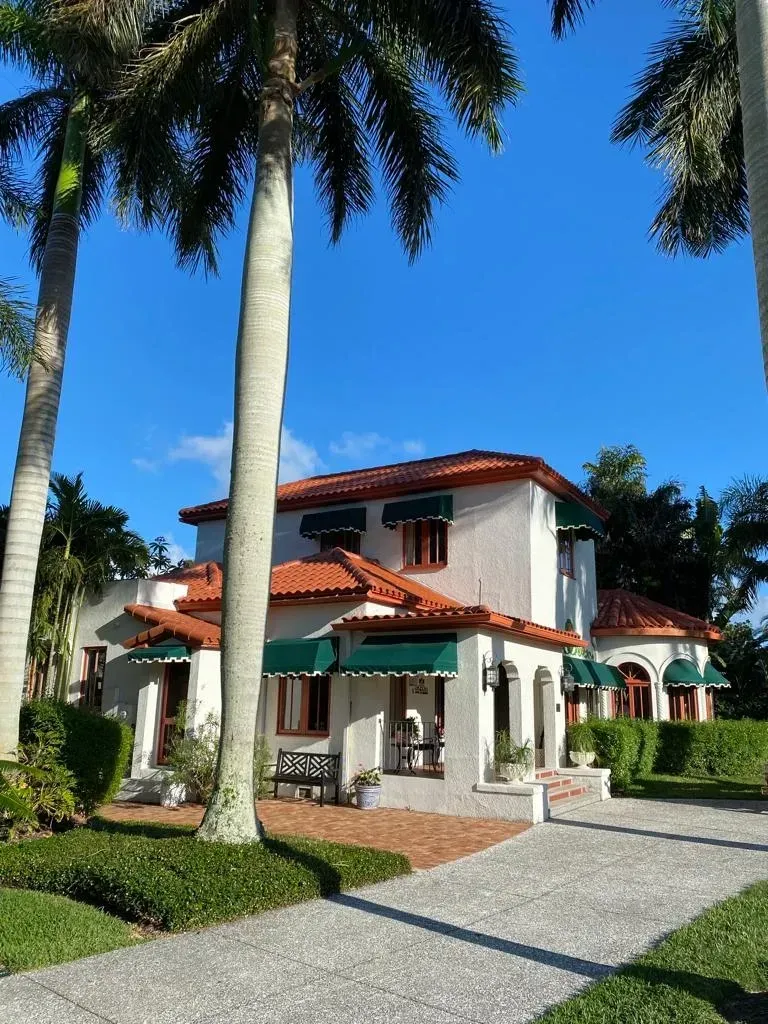 A white house with a red tile roof is surrounded by palm trees