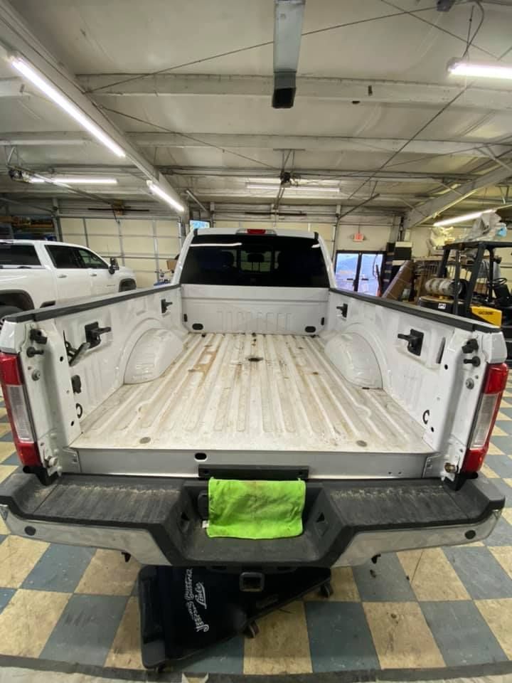 White pickup truck bed, viewed from the rear, inside a shop. A green cloth sits on the bumper.