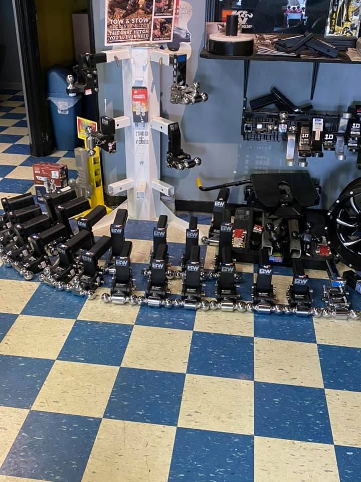 A store displays rows of black trailer hitches on a blue and cream checkered floor.  There's a variety of hitches in the background.
