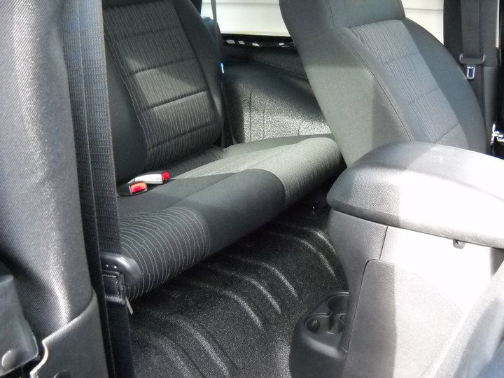 Interior of a black Jeep showing rear seats and a textured black floor. Gray fabric seats contrast with black trim.