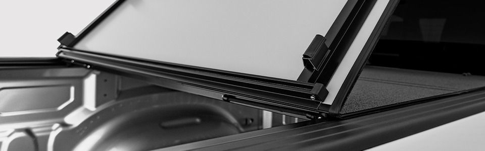 A black and white close-up shows the open lid of a truck bed cover, revealing the bed's interior.