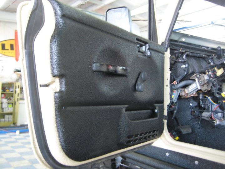 Black textured car door panel open against a beige frame, revealing exposed wires and components.