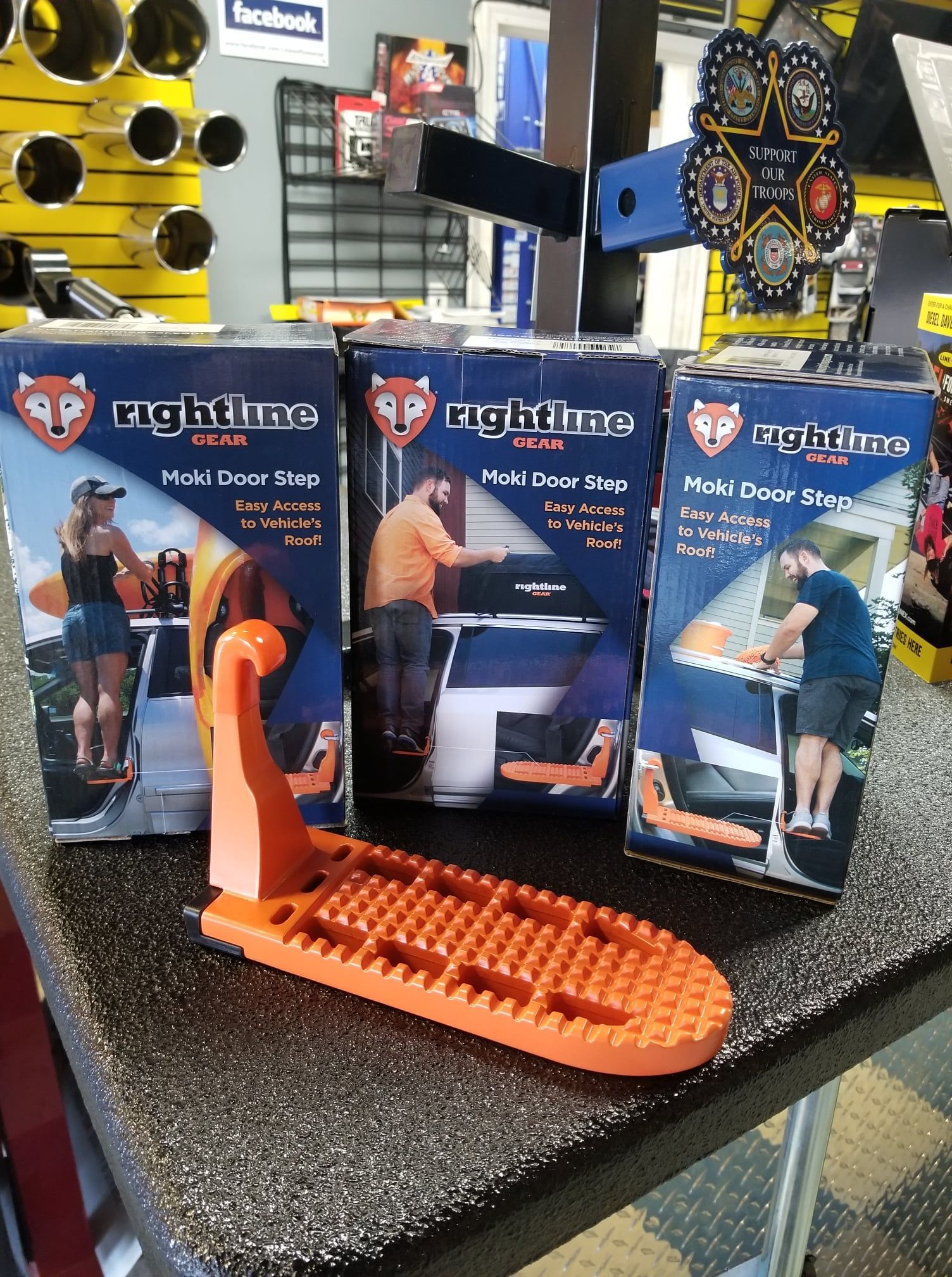 An orange car door step with three boxes showing people using it, displayed on a metallic surface inside a store.