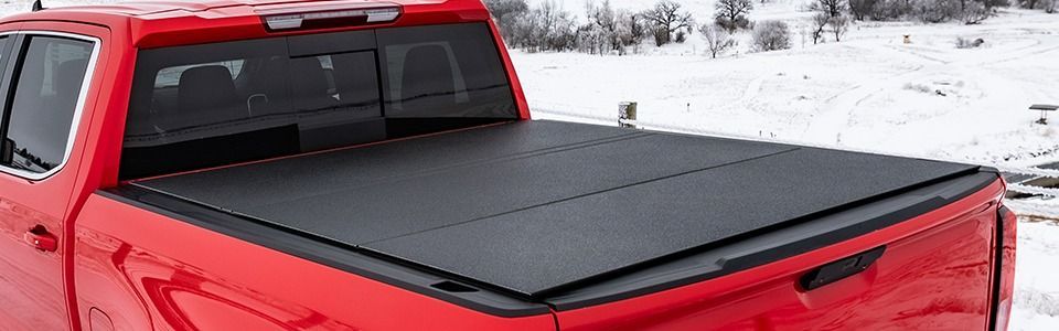Red pickup truck with a black cover over the truck bed in a snowy outdoor setting.
