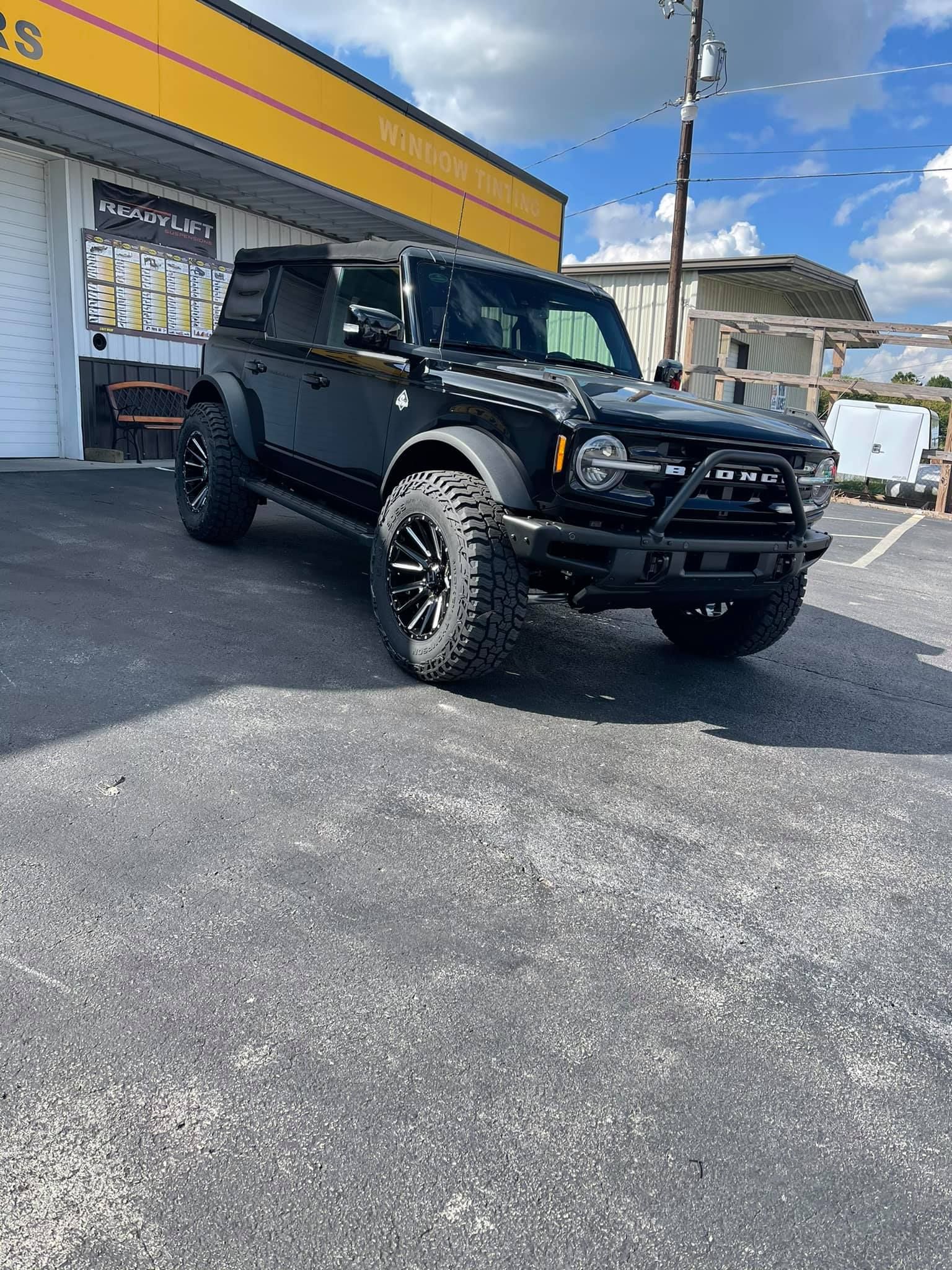 Black Ford Bronco SUV parked in front of a building with large, off-road tires, a front bumper guard, and a black exterior.